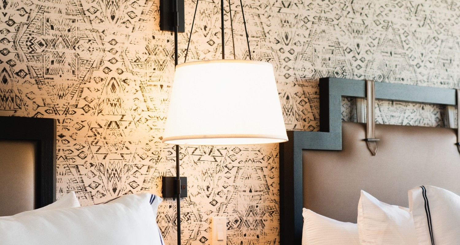 A bedside view of the room including a lamp, nightstand, and an outlet.