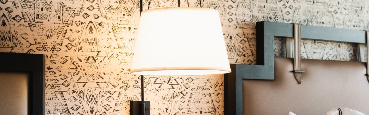 A bedside view of the room including a lamp, nightstand, and an outlet.