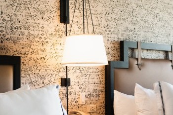 A bedside view of the room including a lamp, nightstand, and an outlet.