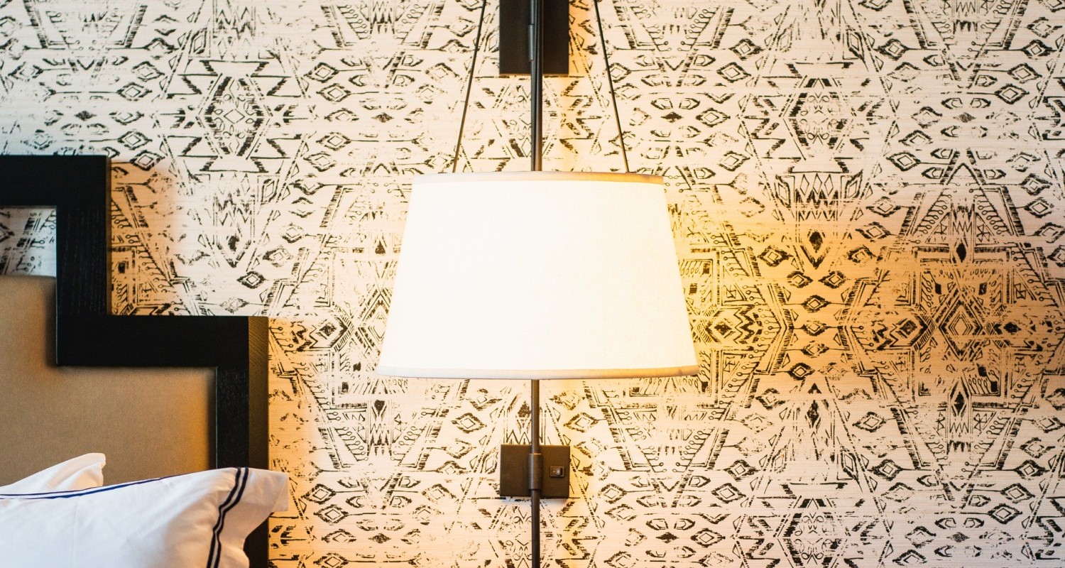 A bedside view of the room including a lamp, nightstand, and an outlet.
