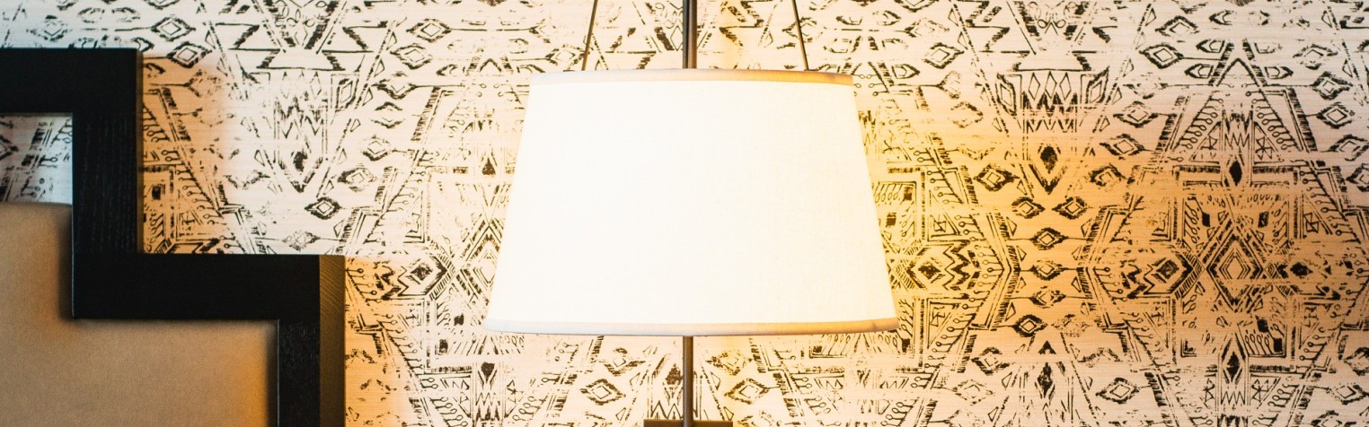 A bedside view of the room including a lamp, nightstand, and an outlet.