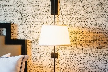 A bedside view of the room including a lamp, nightstand, and an outlet.